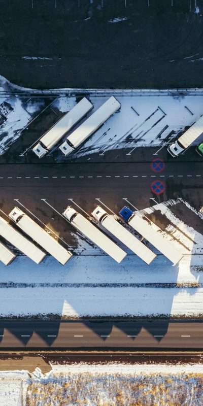 Top-down aerial view of trucks parked in a snowy lot in Poznań, Poland, showcasing winter logistics.